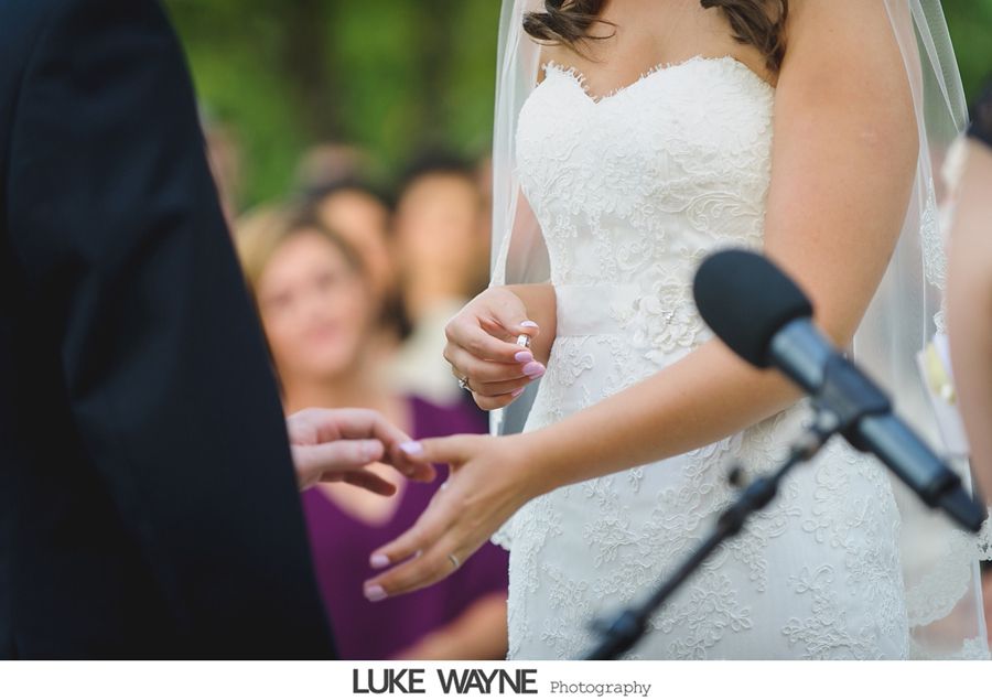 Bride receiving ring during outdoor wedding ceremony. Close up on hands, white dress, microphone.