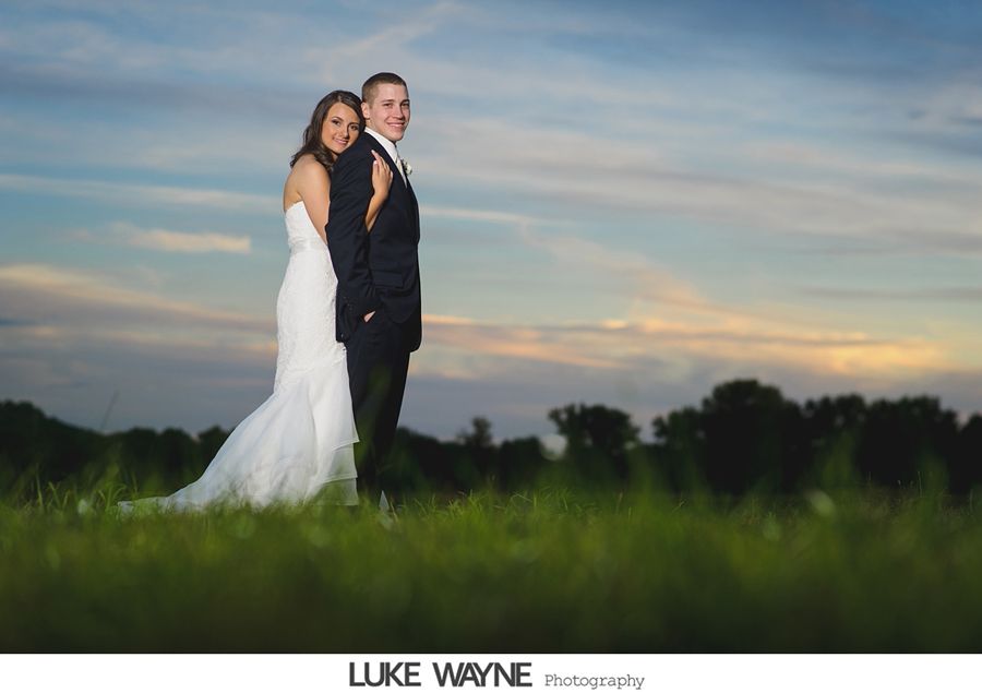 Bride and groom standing back to back in a field at sunset.