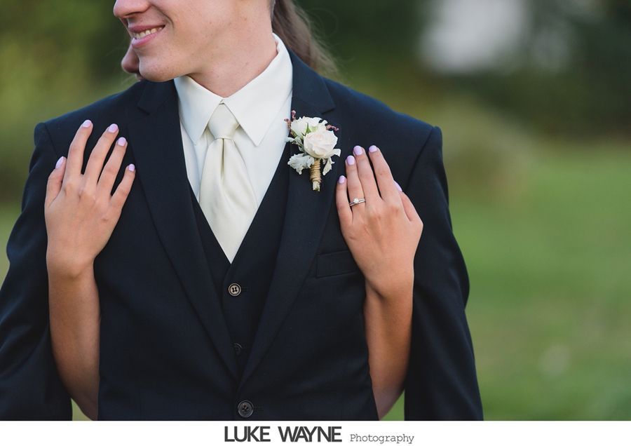 Person in a suit embraced by someone whose hands are on the jacket; boutonniere, ring.