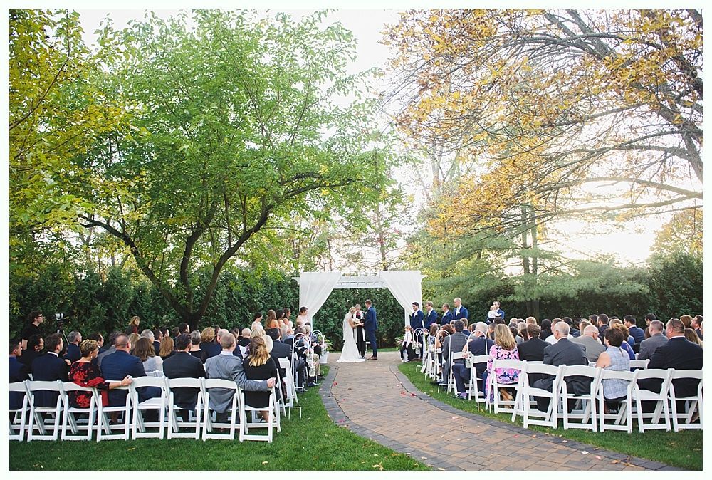 Wedding ceremony outdoors with guests seated, a couple at the altar, pathway to the front.