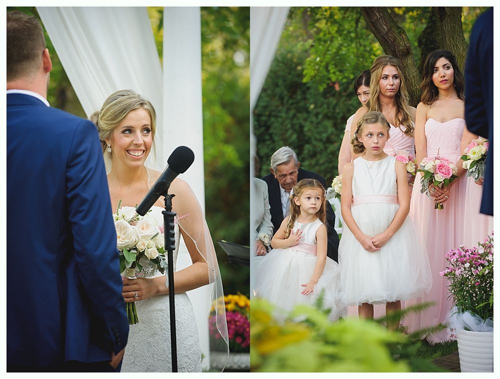 Bride smiling at groom during outdoor wedding ceremony; bridesmaids and flower girls stand nearby.