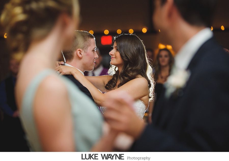 Bride and groom dancing at wedding reception, illuminated by background lights; people watching.