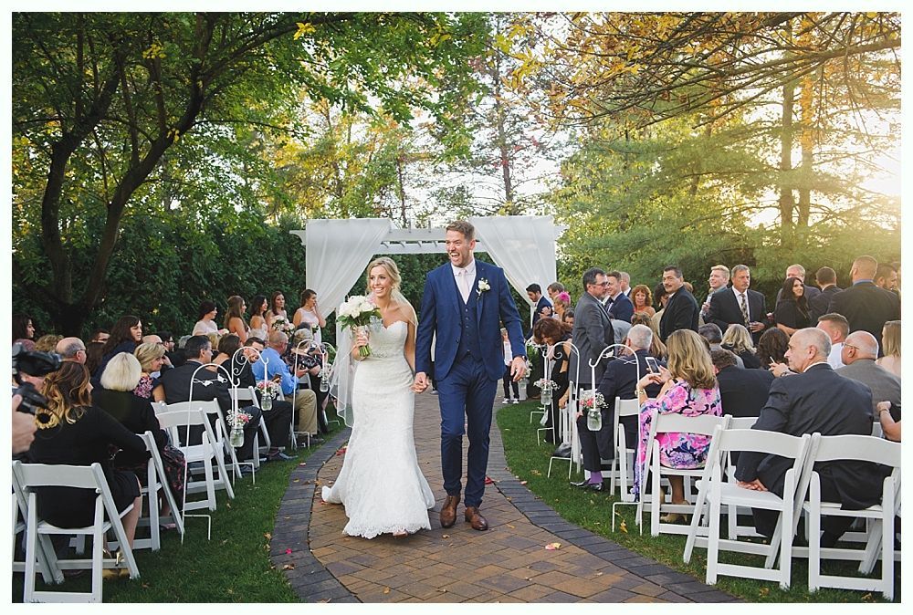 Newlyweds walk down the aisle after their wedding ceremony. Surrounded by guests in an outdoor setting.