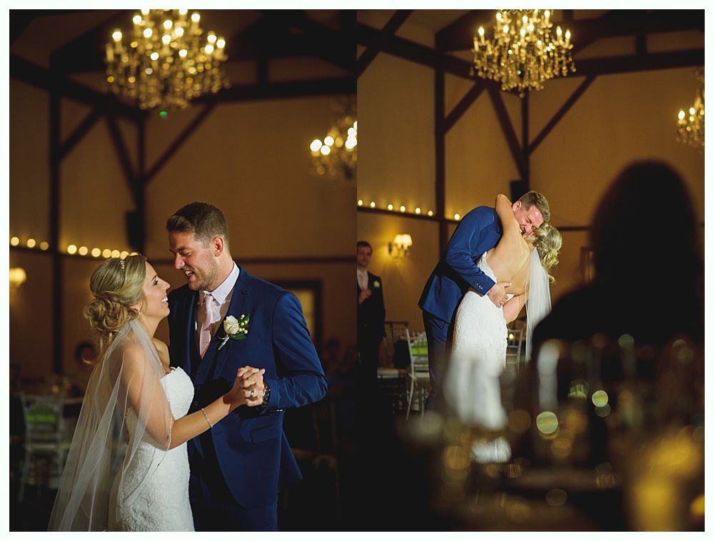 Couple dancing at a wedding reception under chandeliers. The groom in a blue suit, bride in a white dress, embracing and smiling.