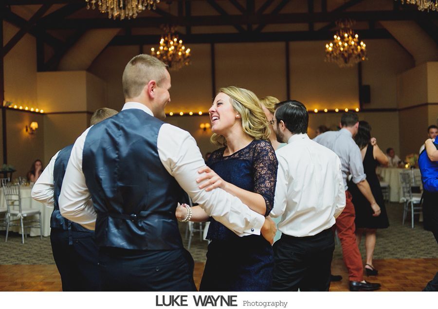 People dancing at a wedding reception; a couple smiles at each other, in a warmly lit ballroom.