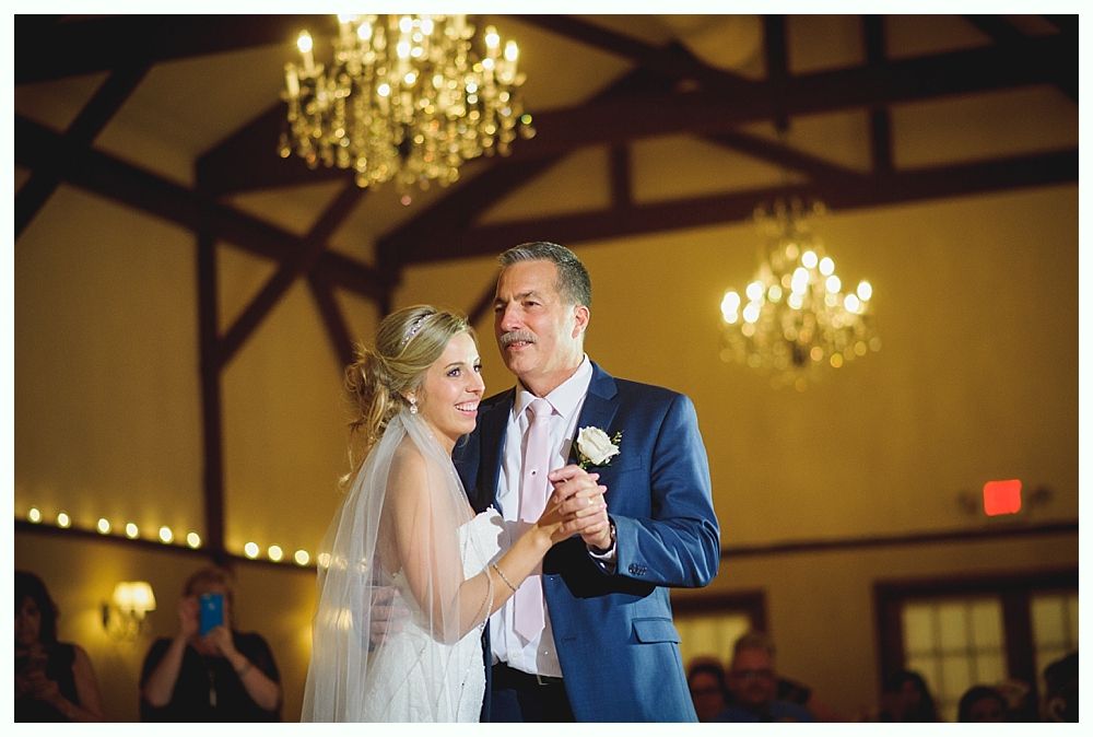 Bride and groom dancing at a wedding reception, holding hands. Soft lighting, chandeliers.