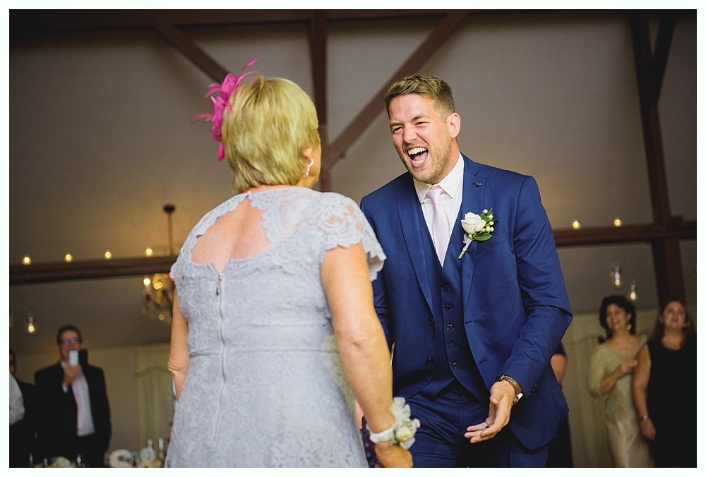 Man in blue suit laughs while dancing with a woman in a gray dress at a reception.