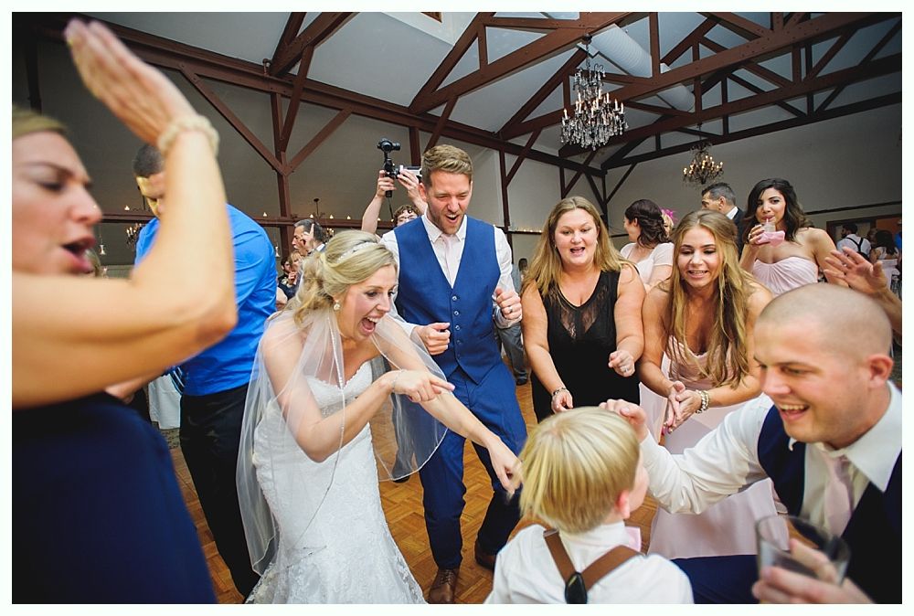 Wedding reception with dancing couple, excited guests in a rustic hall with a chandelier.