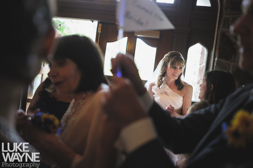Couple embracing outdoors; woman smiles up at man, both in casual wear, near trees.