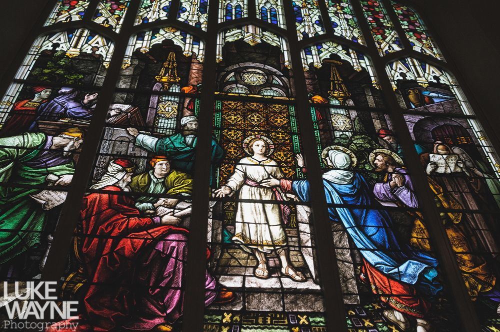 Couple embracing on a rocky peak, with a tower in the background, under a cloudy sky.
