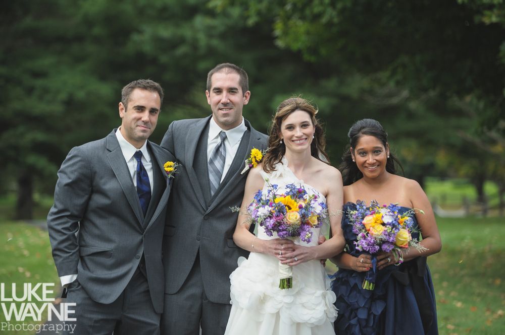 Couple embracing, smiling in front of a tall stone tower with cloudy sky background.