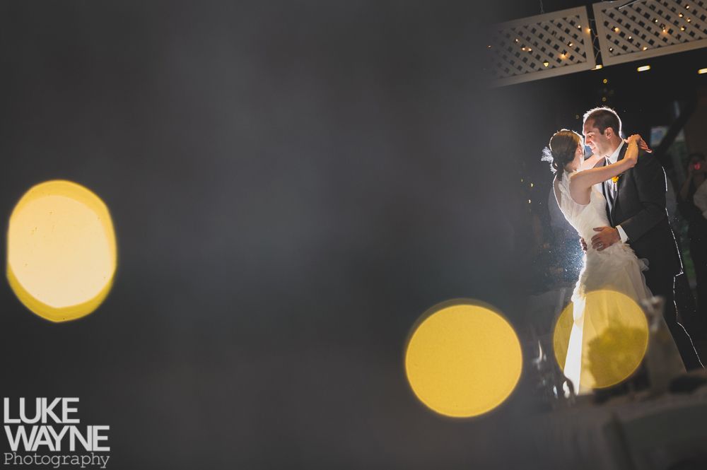 Couple embracing at sunset; man in green shirt, woman in denim jacket and red dress, with blowing hair.