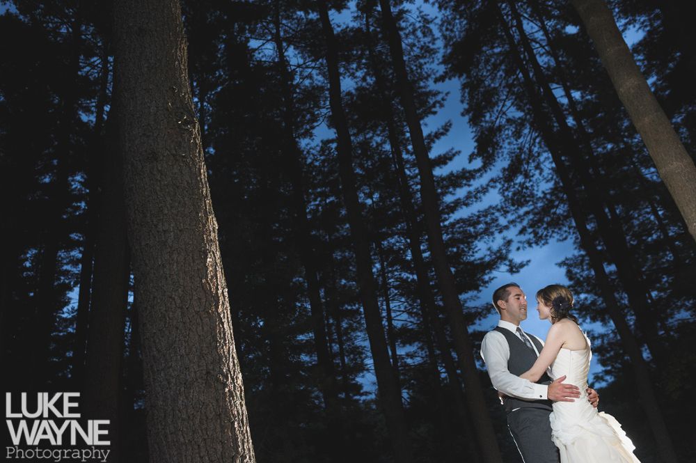 Couple embracing at sunset; man in green shirt, woman in denim jacket and red dress, with blowing hair.