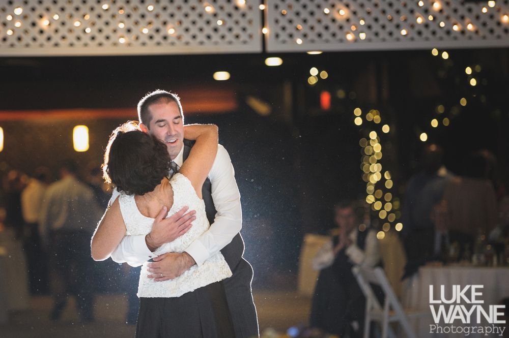 Couple embracing at sunset; man in green shirt, woman in denim jacket and red dress, with blowing hair.
