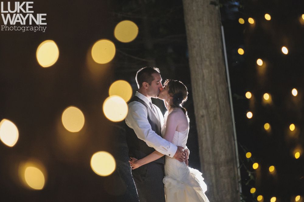 Couple embracing at sunset; man in green shirt, woman in denim jacket and red dress, with blowing hair.
