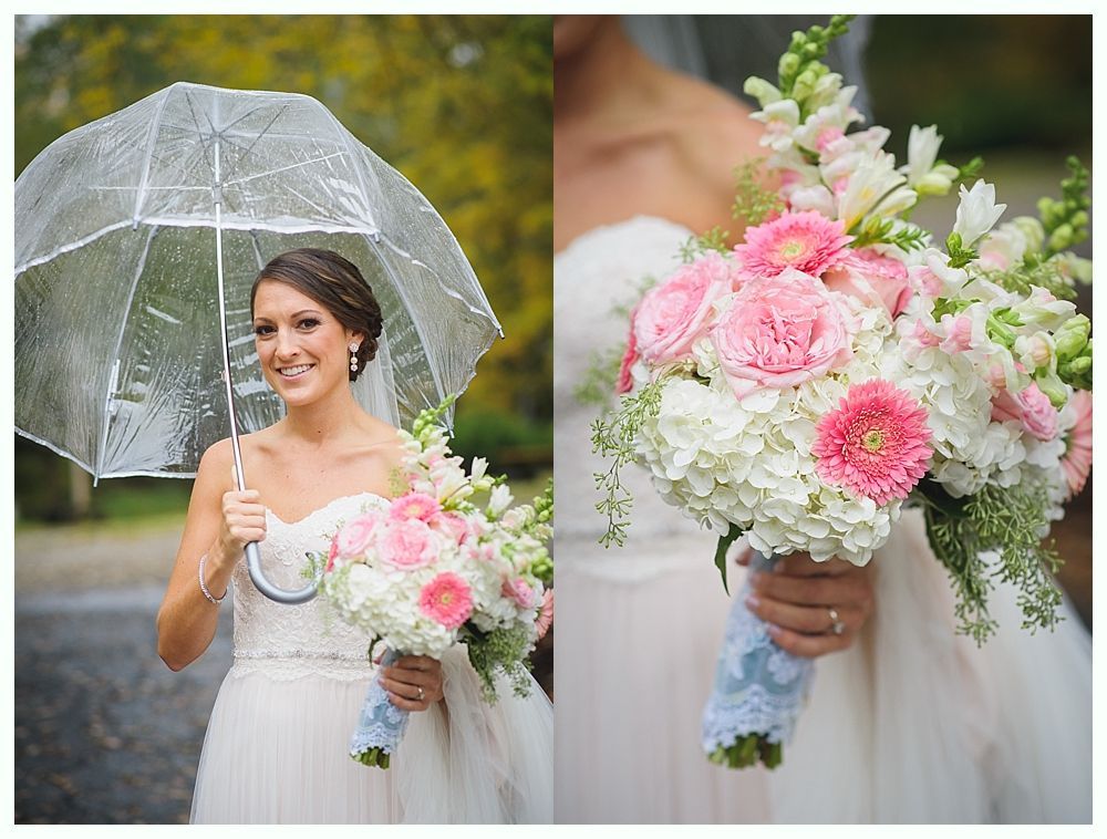 Bride holding flowers and clear umbrella smiles, wearing a strapless gown, outdoors.