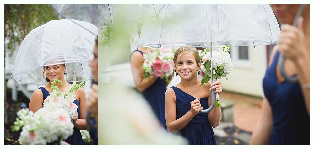 Bridesmaids in navy dresses holding bouquets under clear umbrellas on a rainy day.