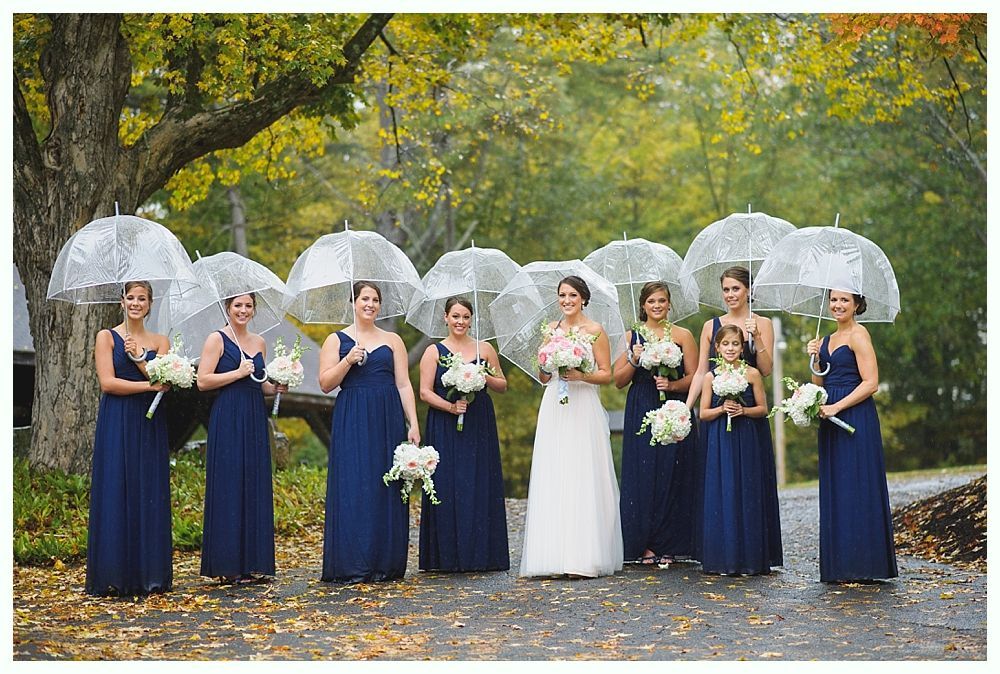 Bridesmaids and bride in navy dresses, holding bouquets and clear umbrellas. Outdoor wedding.