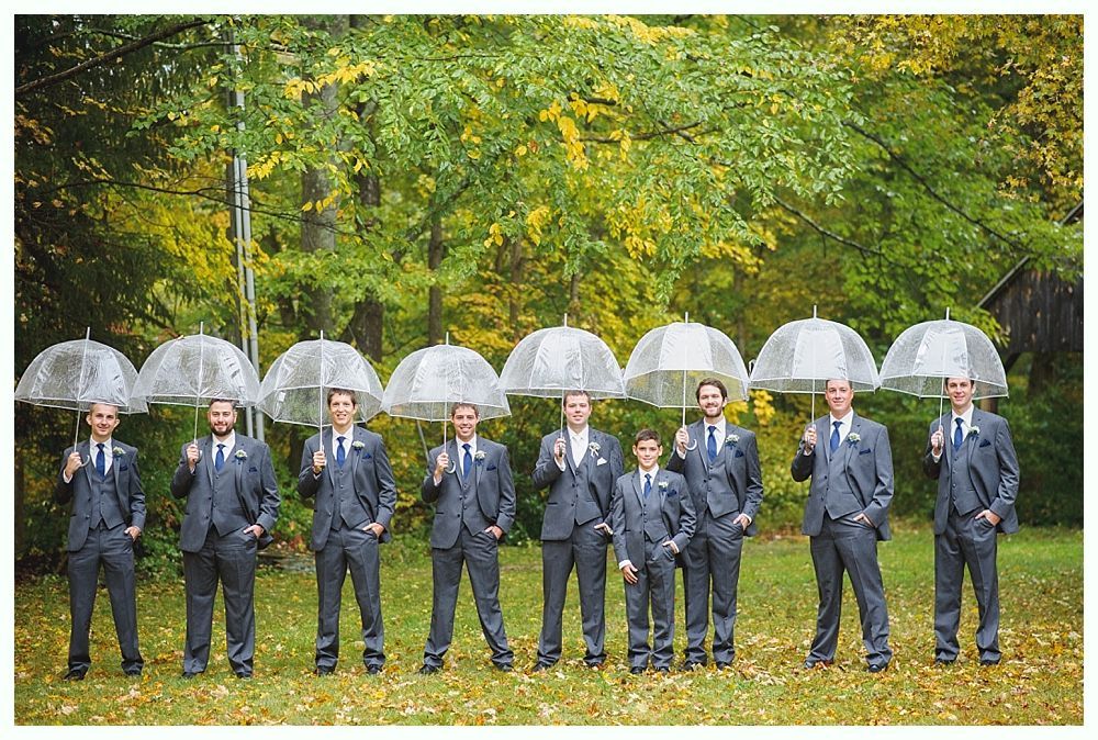 Men in gray suits stand in a row, holding clear umbrellas under a yellow and green tree backdrop.