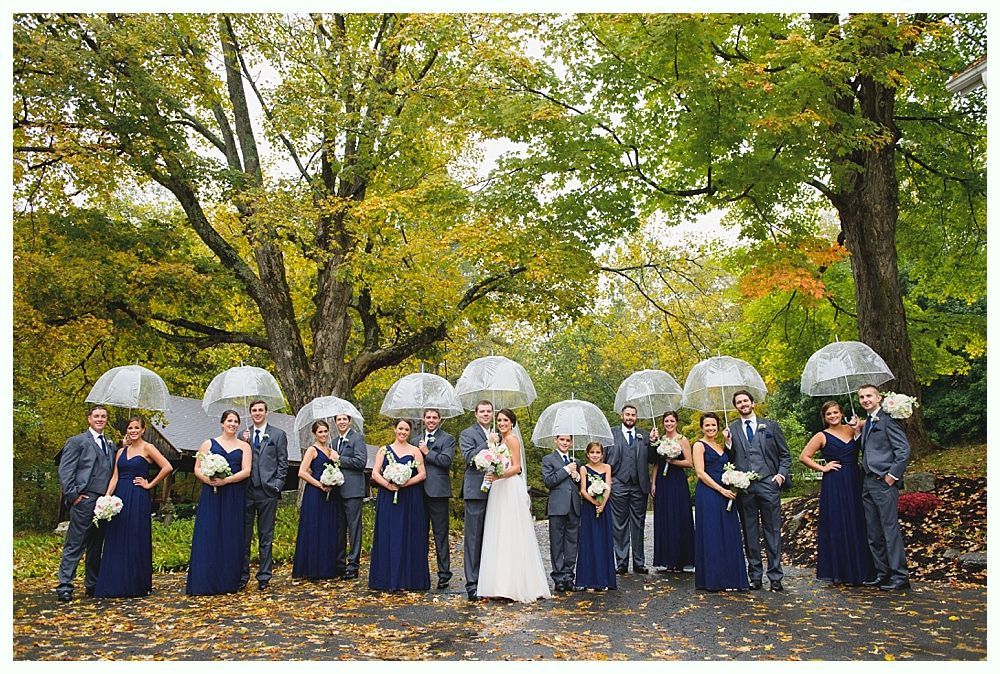 Wedding party poses with umbrellas outdoors under autumn trees.