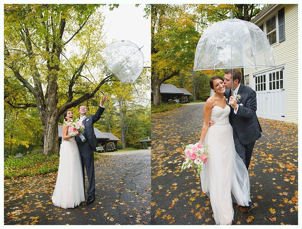 Bride and groom under a clear umbrella on a fall day. They are standing on a paved driveway near a house.