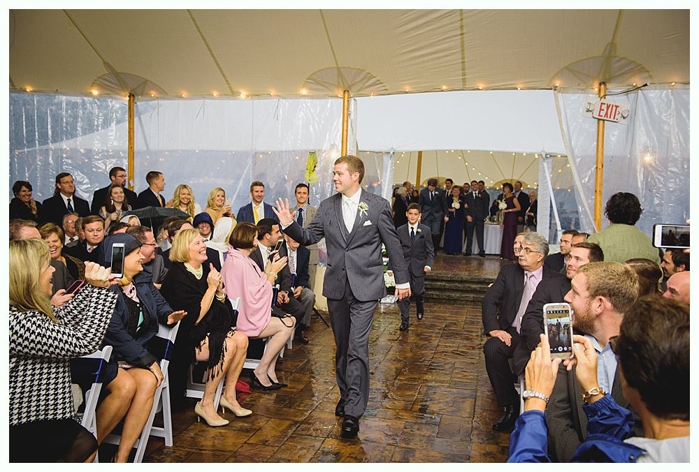 Groom waves as he walks down the aisle, cheered on by wedding guests in a tent.