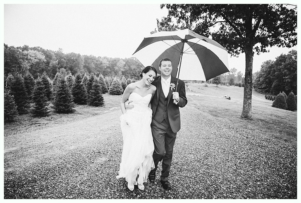 Bride and groom walk under an umbrella in a field. Black and white photo.