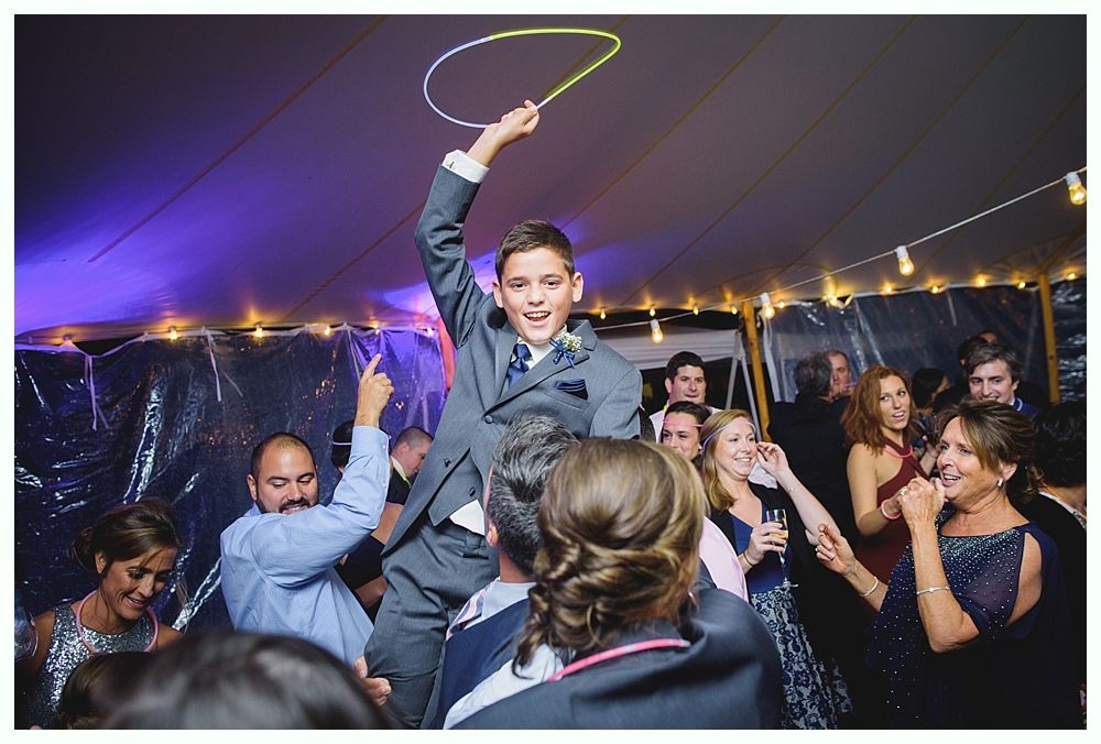 Boy in suit on shoulders, holding glow stick, celebrating at party with people.