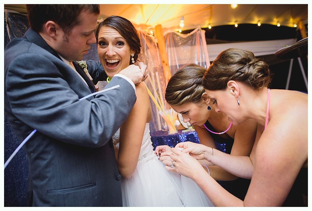Wedding party: Bride in white gown being helped by two women and a man, all smiling.