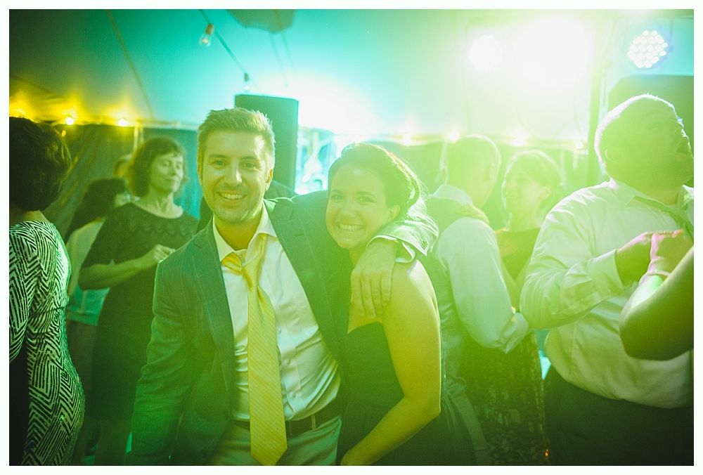 Couple smiles, arm around each other, dancing at an event with bright green and yellow lighting.