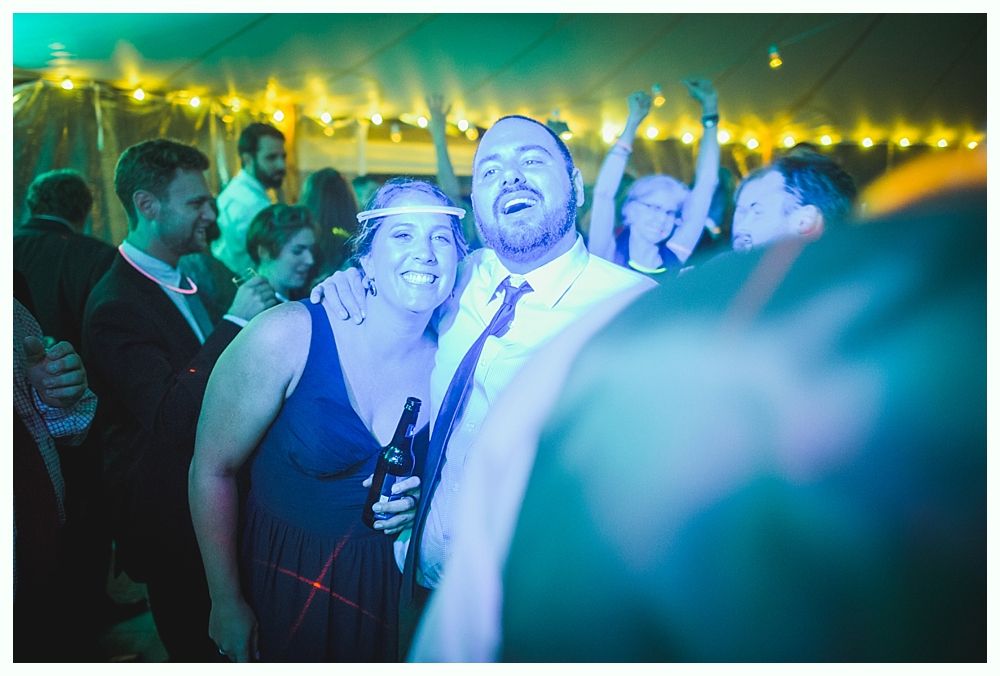 Couple smiling at a party, illuminated by blue and green lights. People in background with raised arms.