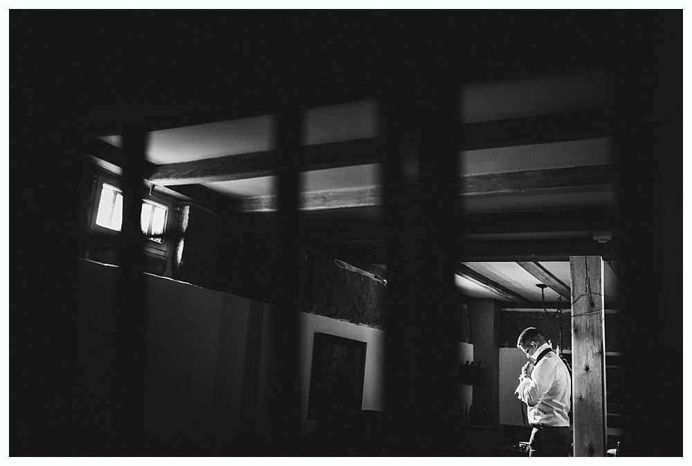 Couple embracing and walking in a grassy field, next to pink wildflowers; trees in the background.