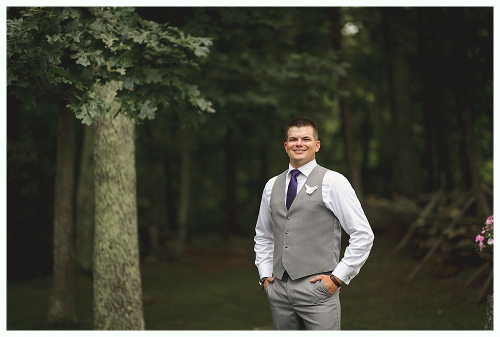 Couple embraces, leaning against a wooden structure; man with a bun, woman with blonde hair, dark background.