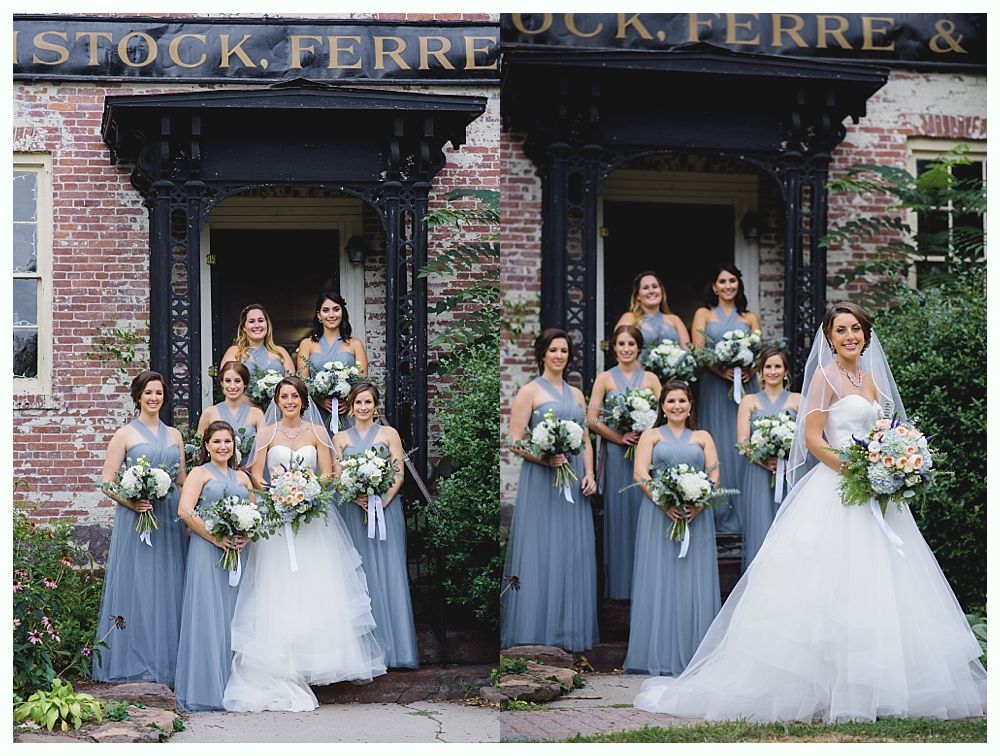 Bridesmaids in blue dresses and bride in white dress pose in front of a building with dark trim.