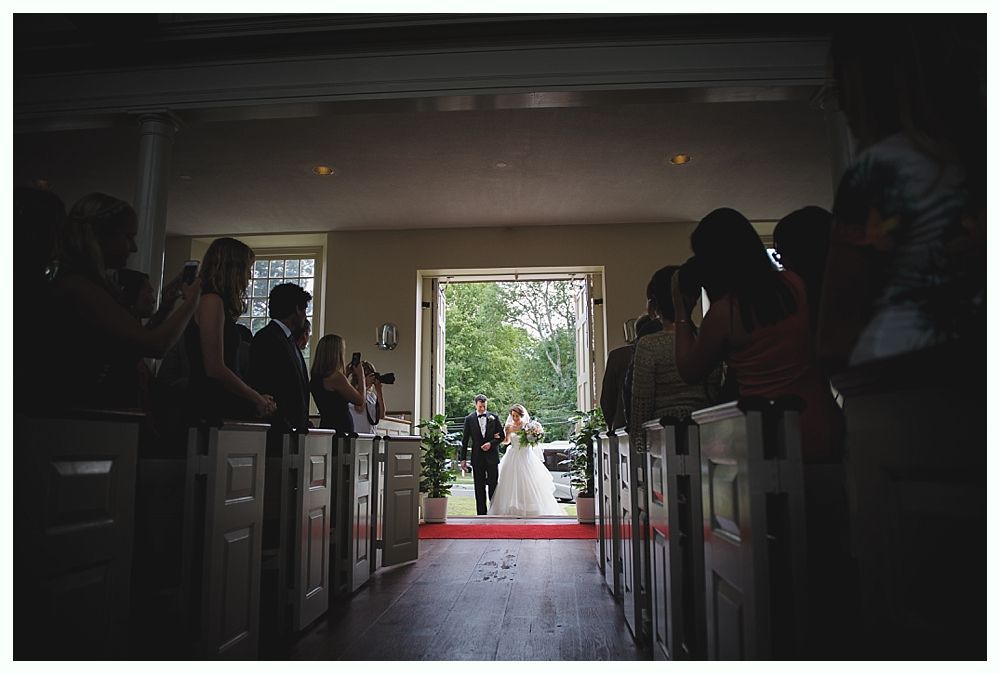 Bride and groom walk down the aisle after their wedding ceremony. Guests watch from pews in a church.