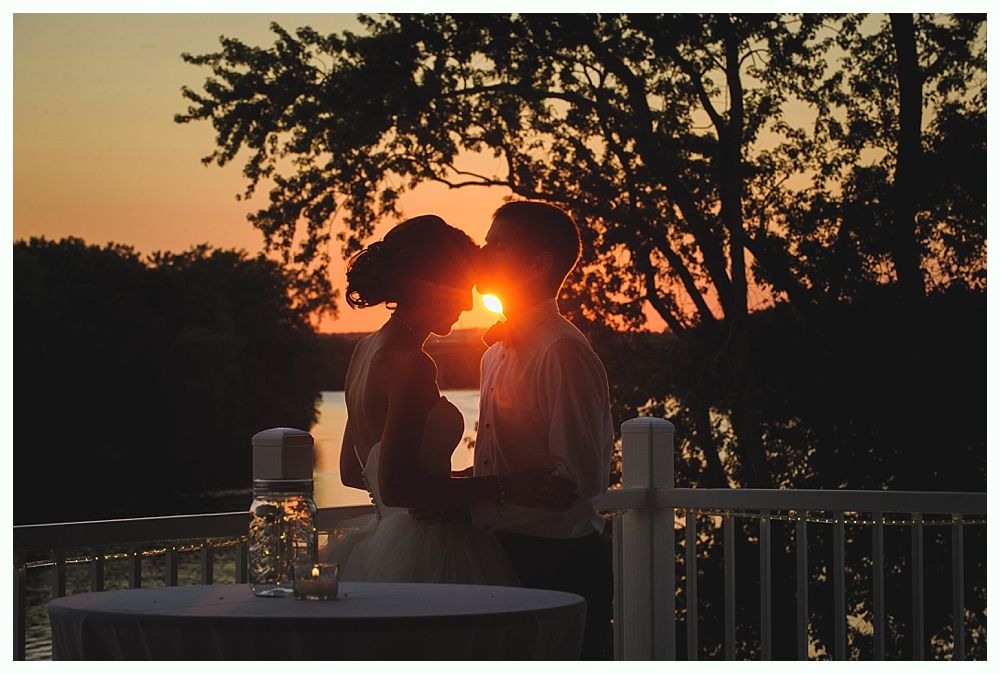 Couple kissing silhouetted against a sunset over water.