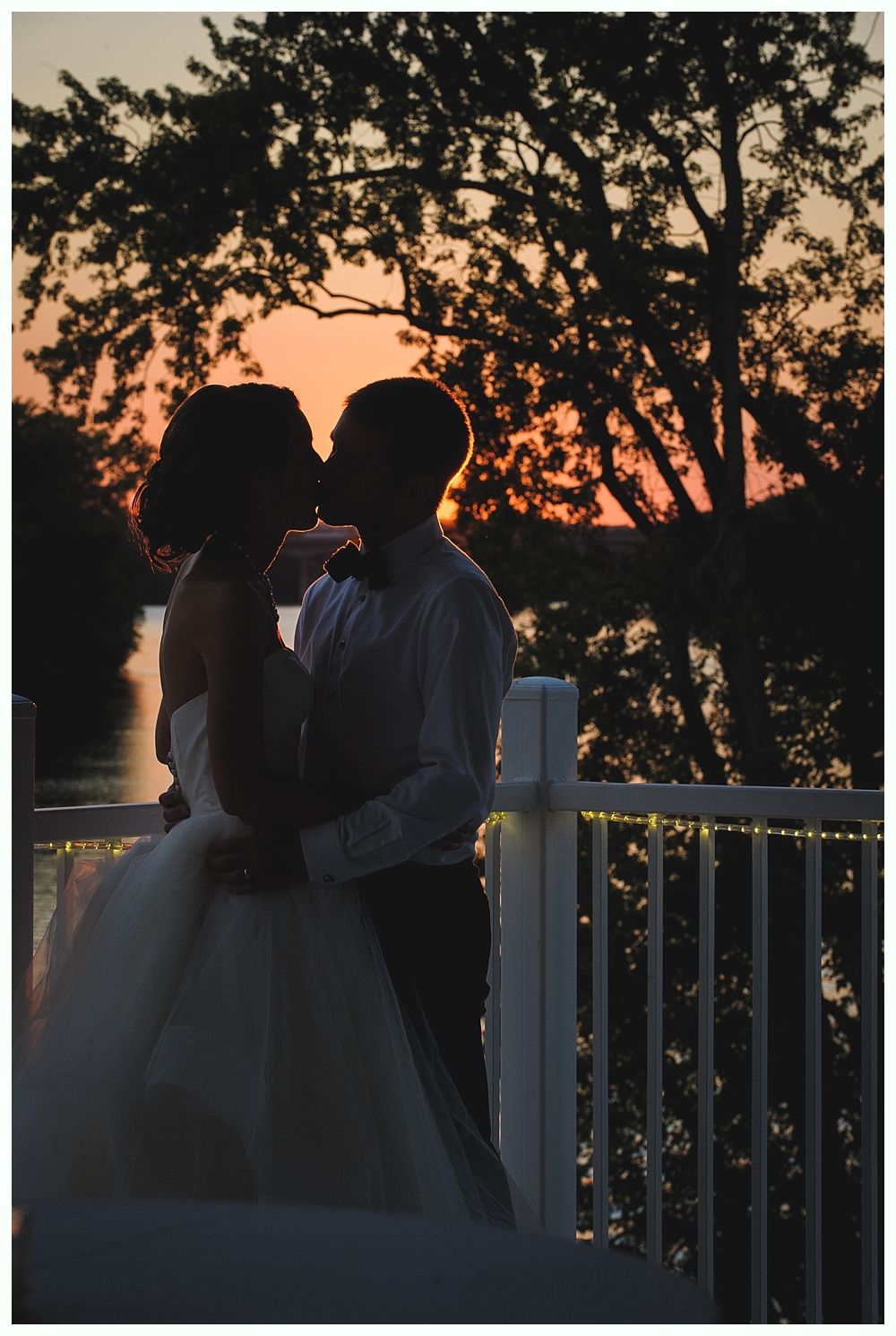 Couple kissing at sunset on a deck. Silhouette of the tree and sky in the background.