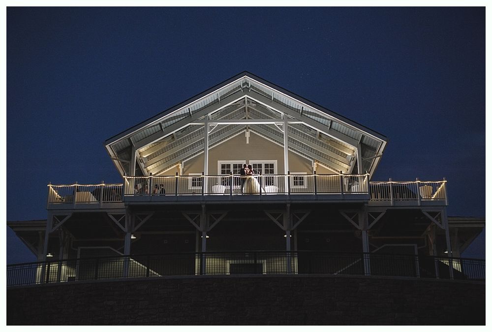 Couple on a balcony, illuminated barn at night with string lights, clear sky.