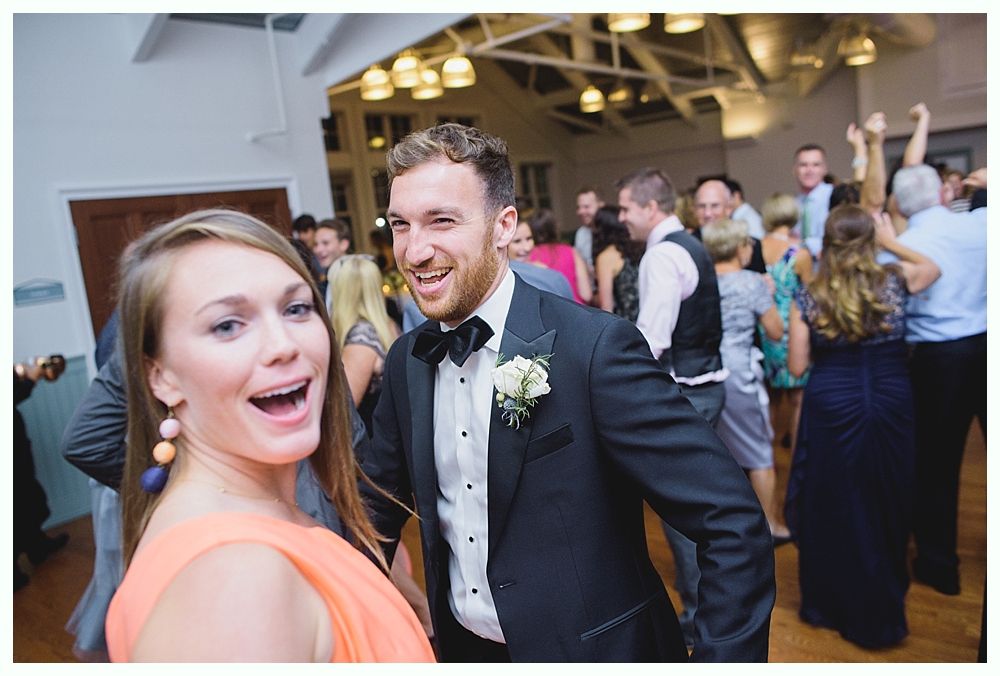 People dancing at a wedding reception. Woman in orange dress and man in tux winking at camera.