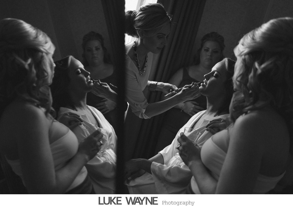 Woman having makeup applied with two bridesmaids reflected in mirror.