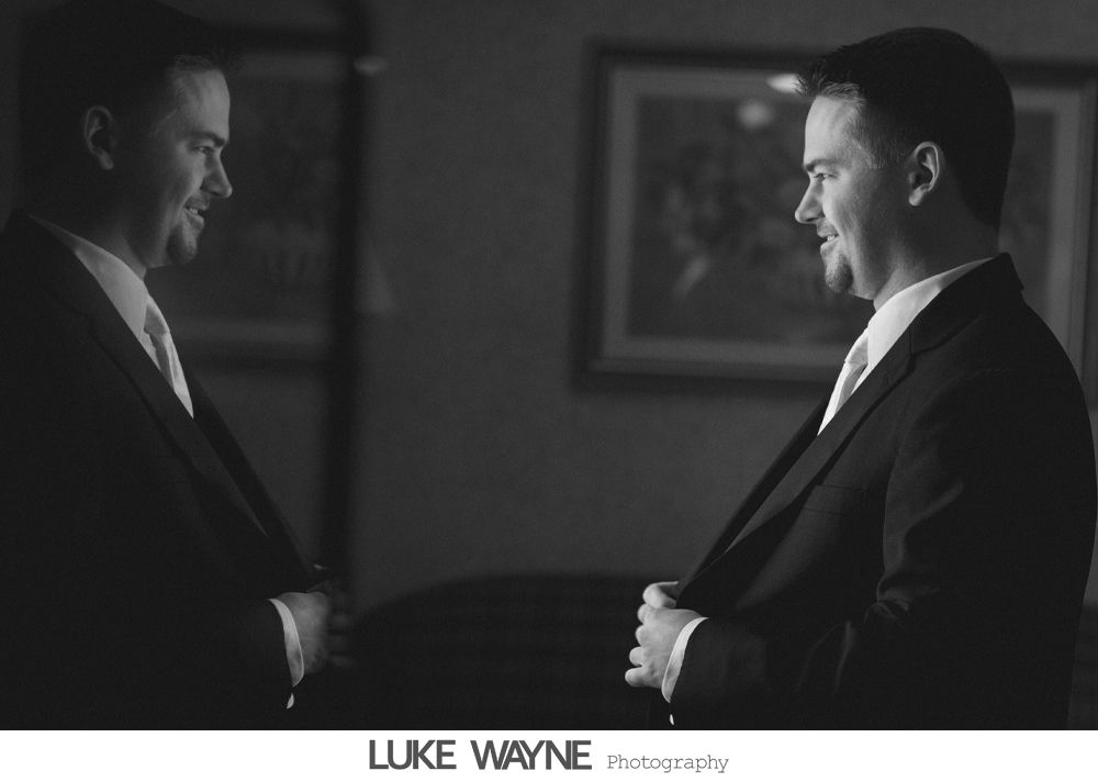 Man in suit adjusting jacket, reflected in a mirror. Black and white photo.