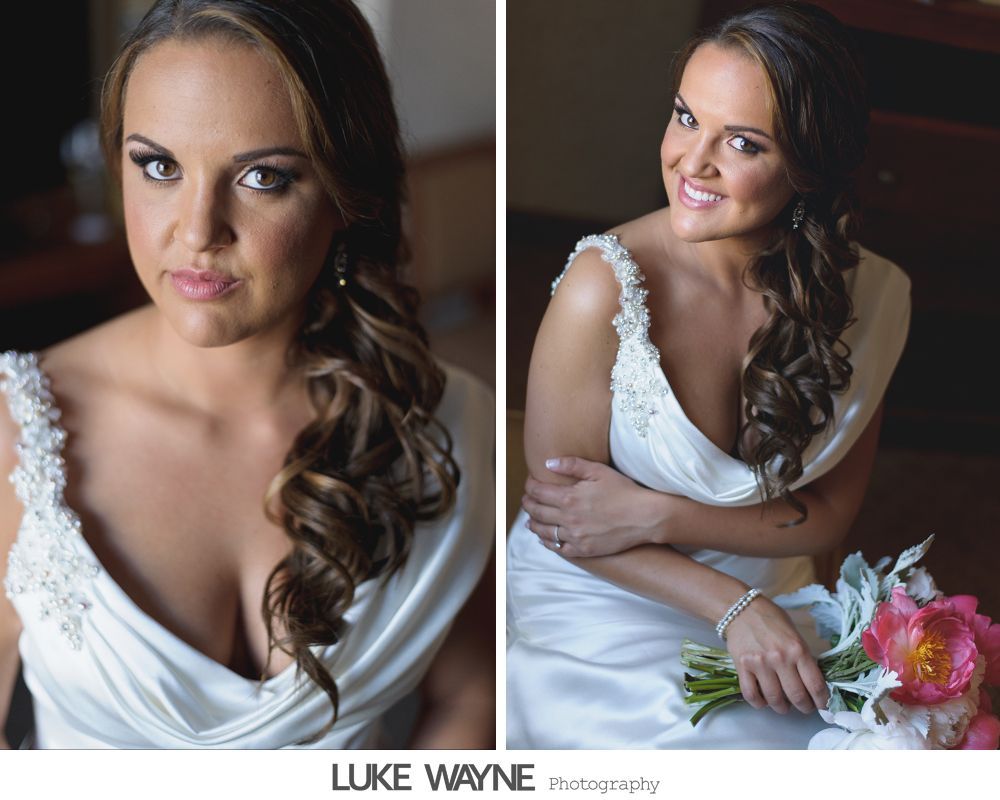 Bride in white wedding dress with curly side-swept hair, holding a bouquet, looking at camera.