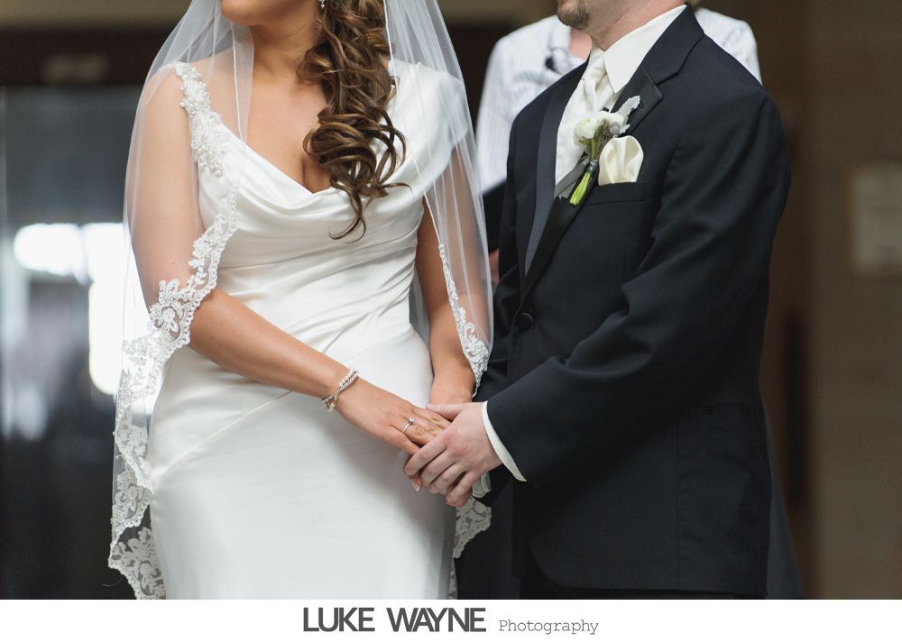 Bride and groom holding hands during a wedding ceremony. Bride wears a white dress and veil, groom a black suit.