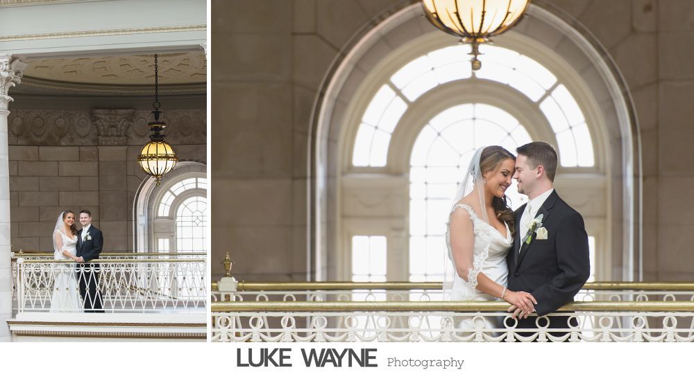 Bride and groom smiling, posing on a balcony with a large arched window in the background.