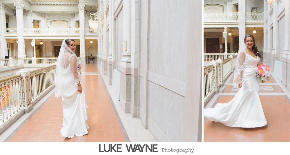 Bride in white wedding dress with a veil and bouquet poses in a bright, ornate hallway.