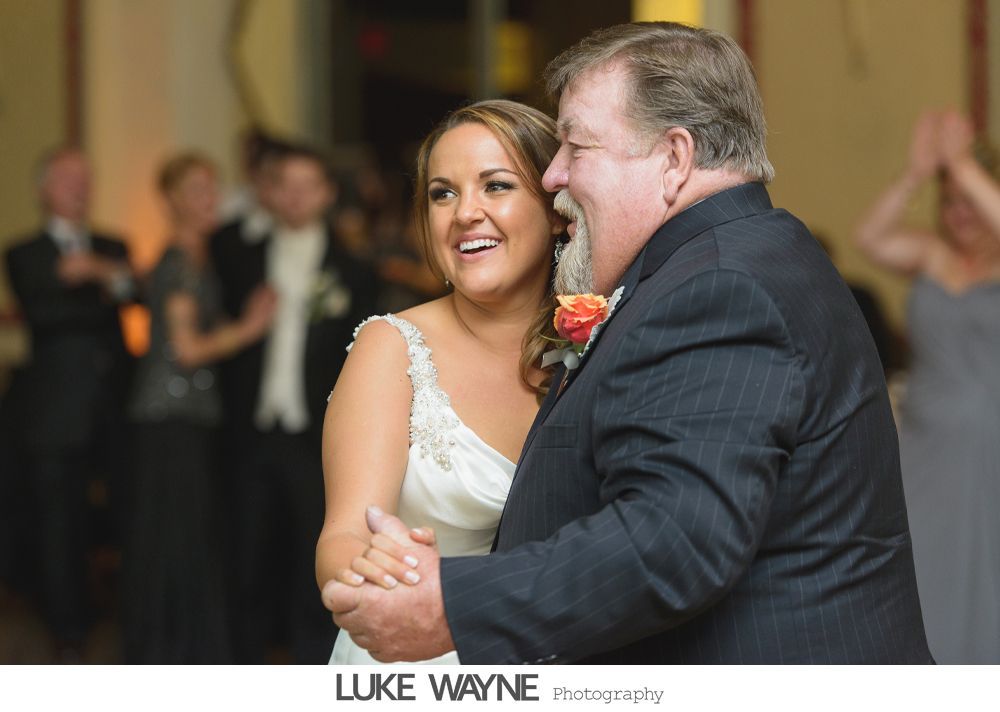 Bride dancing with a man in a dark suit, both smiling, inside a venue.