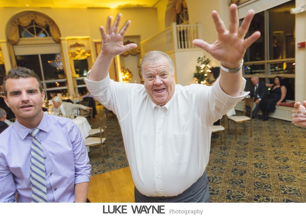 Man with arms raised, smiling, next to another man in a room with tables and a staircase.