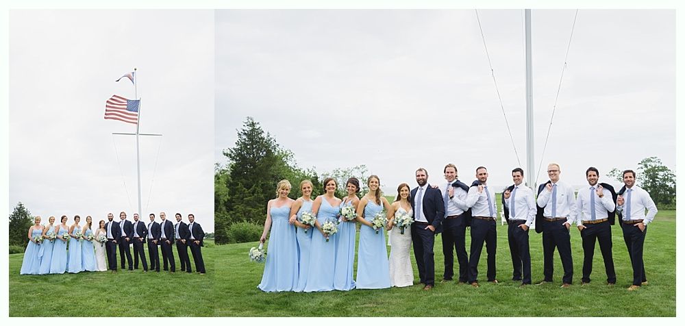 Wedding party in light blue and navy attire posing on a grassy field with American flag in background.