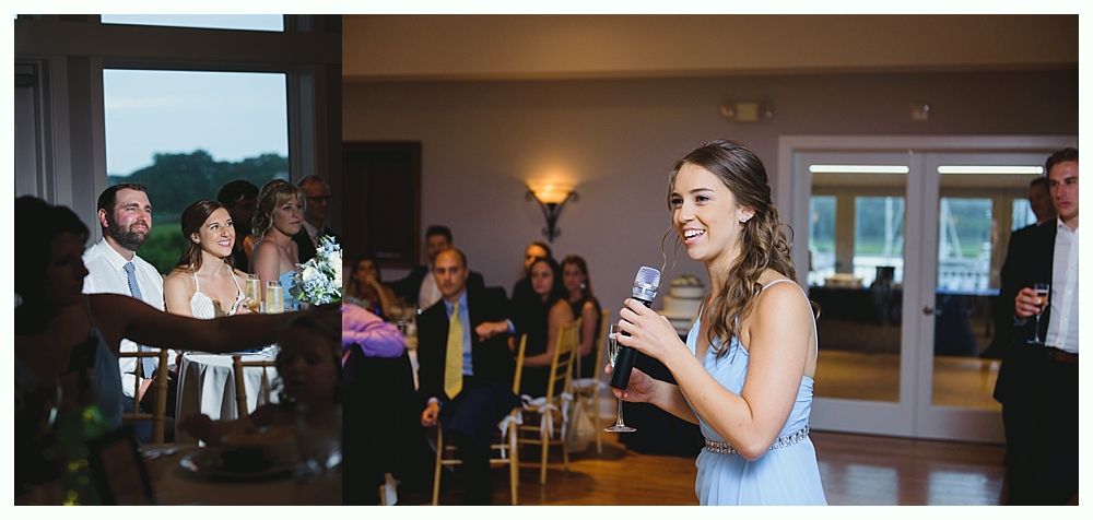 Woman in blue dress giving a speech at a wedding, smiling, holding microphone. Guests in background.