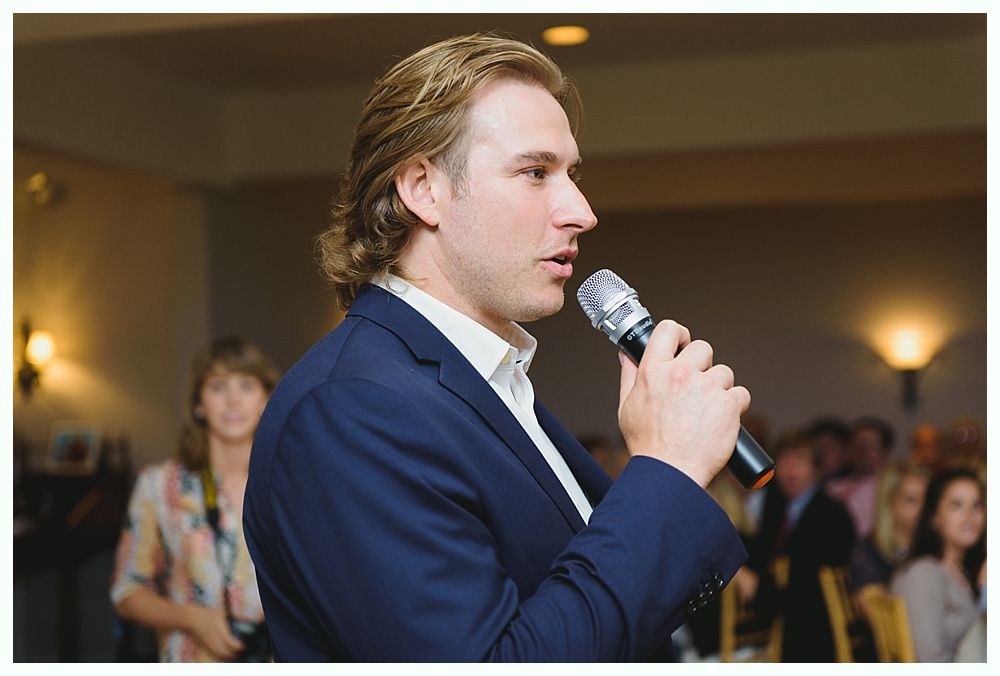 Man in blue blazer speaks into microphone at an event.